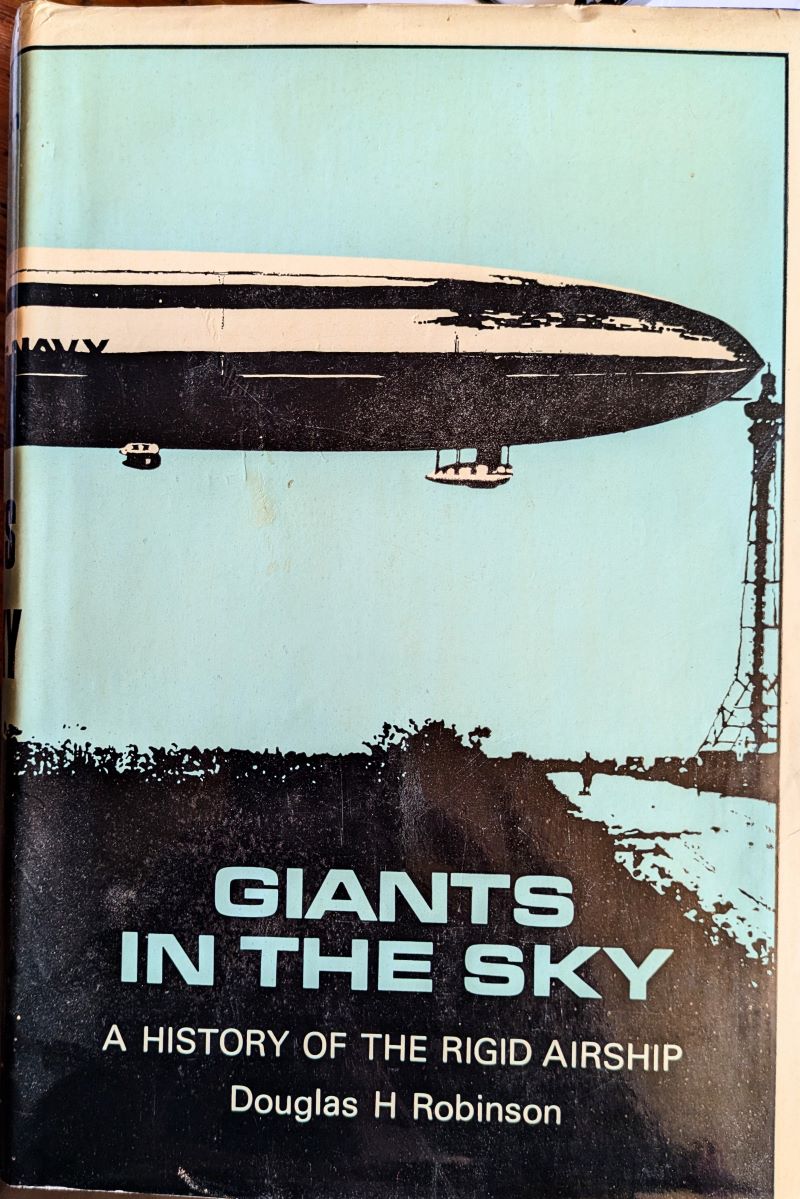 Picture of book cover showing the front half of a large airship floating whilst attached to a mooring mast against a blue backgroind.